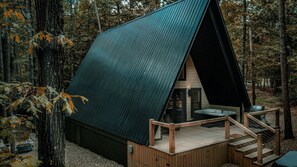 A cabin with a sloped roof, a deck with stairs, and a hot tub.
