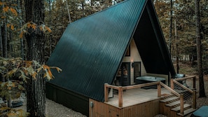 Une cabane avec un toit en pente, une terrasse avec des escaliers et un jacuzzi.