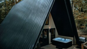A modern, A-frame cabin with a hot tub and a grill area.