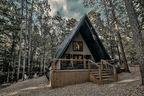 Une cabane avec un toit en pente, une terrasse en bois et une grande fenêtre.