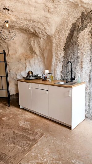 A kitchen with a stone wall, a wooden countertop, a sink, and a hanging light fixture. - Charming Cave near Incredible Outdoor Activities for an Amazing Adventure in Moab, Utah (Moab)