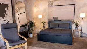 Un dormitorio con cama, una silla, una mesita de noche, una lámpara y una planta en maceta.