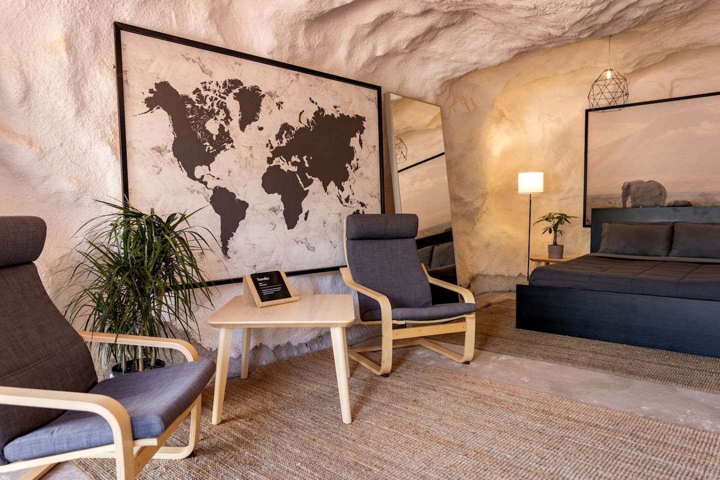 A room with a world map, two armchairs, a small table, a bed, and a lamp.