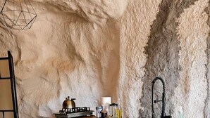 Une cuisine avec un mur en pierre, un plan de travail en bois, un évier et un luminaire suspendu.