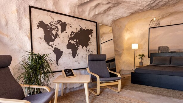 Une pièce comprenant une carte du monde, deux fauteuils, une petite table, un lit et une lampe.
