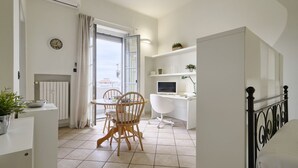 A modern, well-lit room with a dining table, chairs, a desk with a computer, and a bed.