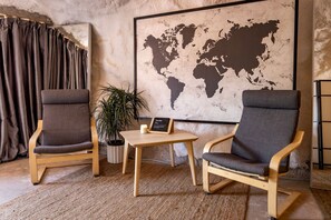 Een kamer met twee houten stoelen, een klein tafeltje, een potplant, een wereldkaart aan de muur en een gordijn.