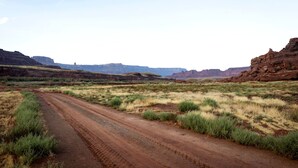 A dirt road in a desert landscape with sparse vegetation and distant mountains.