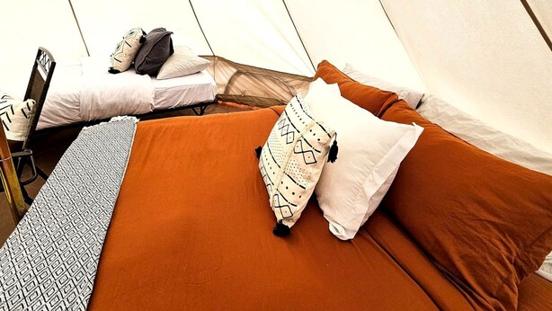 A tented accommodation with two beds, each with pillows and a blanket.