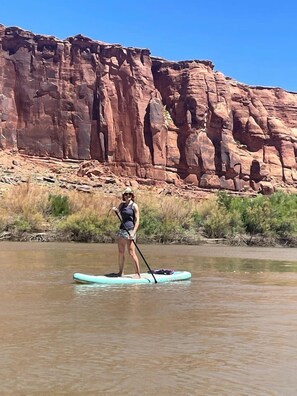 A person paddleboarding on a calm river with a rocky cliff in the background. - Stunning Family Glamping Tent for a True Outdoor Experience on a Secluded Ranch in Moab, Utah (Moab)