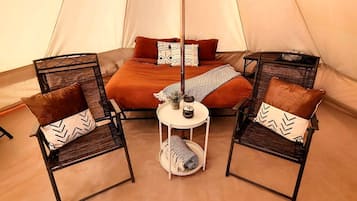 A tent with a bed, two chairs, a small table, and a floor lamp.