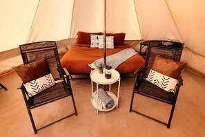 A tent with a bed, two chairs, a small table, and a floor lamp.