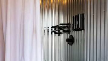 A bathroom with a white toilet, a shower with a black hose, and a metal wall.