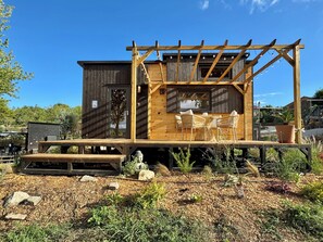 Uma cabana de madeira com varanda, área de estar ao ar livre e um jardim.