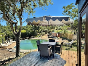 A wooden deck with a pool, lounge chairs, and a table with chairs.