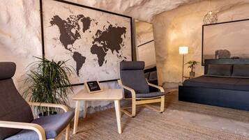 A room with a world map, two armchairs, a small table, a bed, and a lamp.