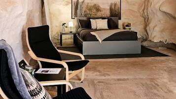A bedroom with a bed, a bedside table, a chair, and a wall-mounted light fixture.
