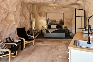 A bedroom with a bed, bedside tables, a chair, a mirror, and a sink.
