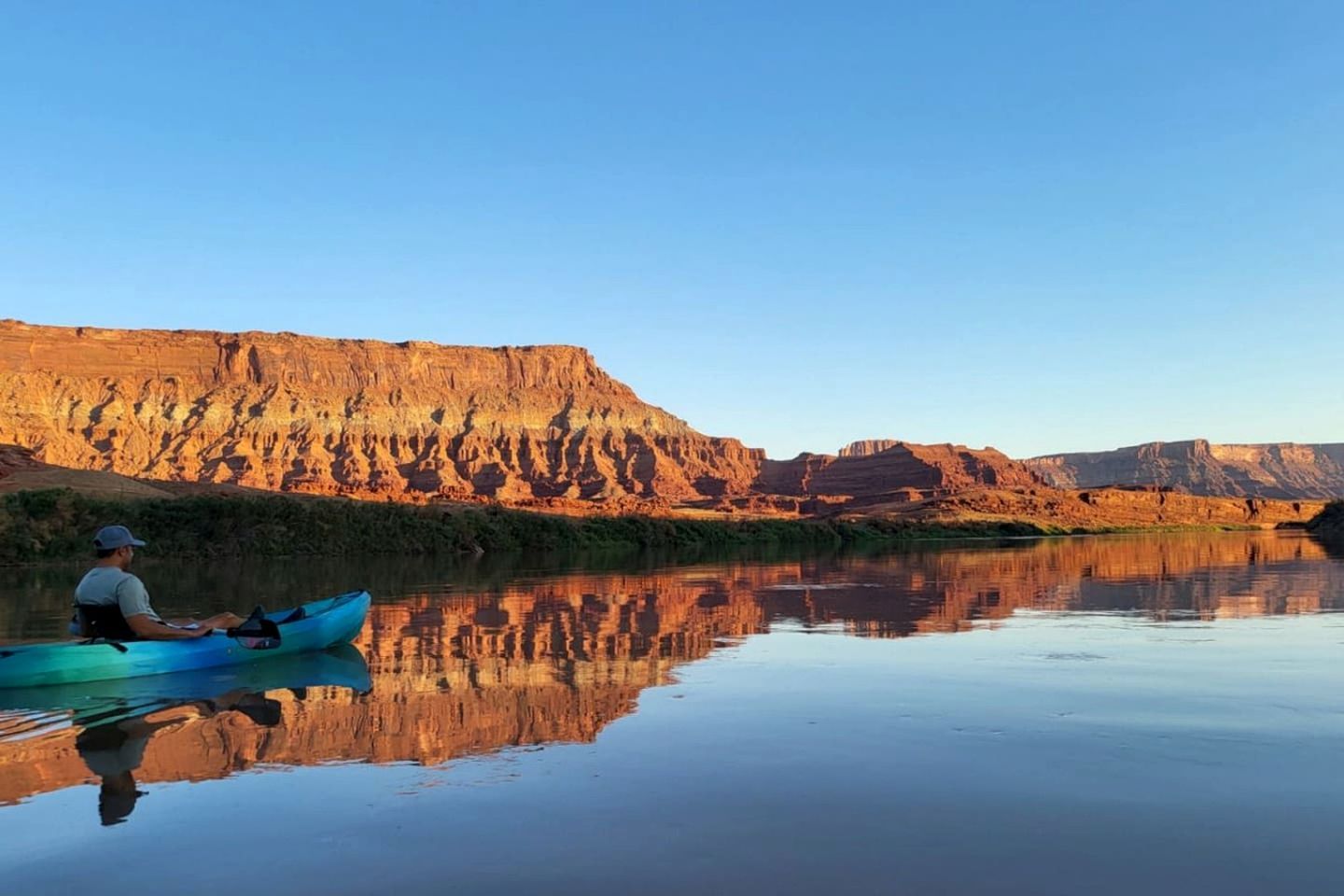 A calm river with a kayaker, reflecting the surrounding cliffs.