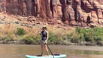 Une personne fait du paddle sur une rivière paisible, avec une falaise rocheuse en arrière-plan.