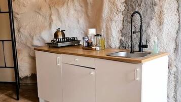 Una cocina con pared de piedra, encimera de madera, pileta y lámpara colgante.
