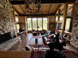Una sala de estar acogedora con chimenea de piedra, muebles de madera y ventanas amplias con vistas al exterior.