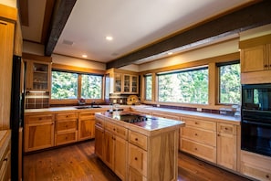 A spacious kitchen with wooden cabinets, a central island, and large windows offering views of greenery.