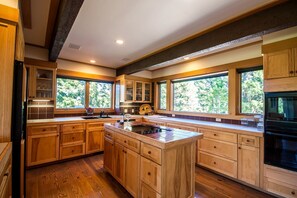 A spacious kitchen with wooden cabinets, a central island, and large windows offering views of greenery.