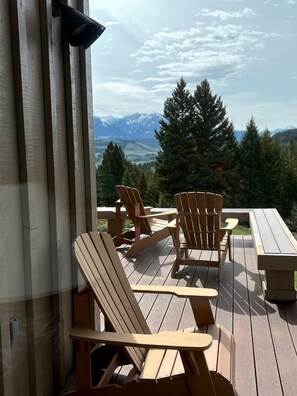 A deck with wooden Adirondack chairs and a picnic table overlooking a mountainous landscape.