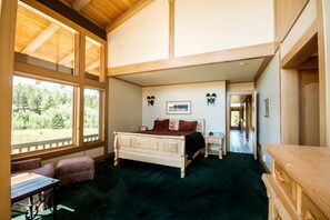 A bedroom with a large window, a bed, a desk, and a chair.