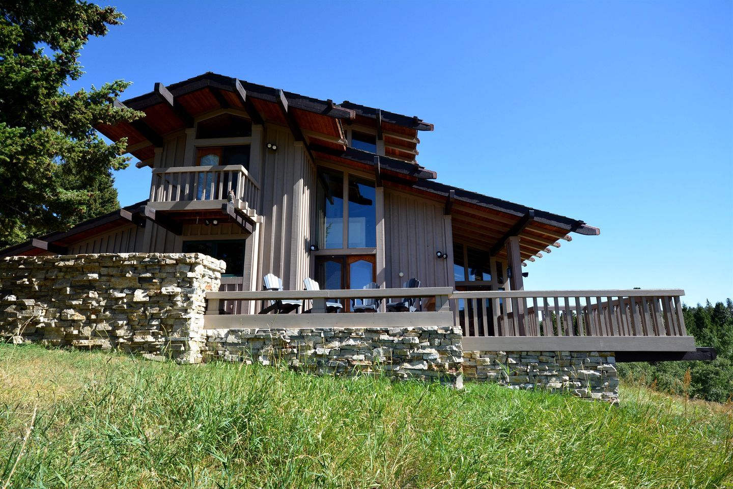 A large, multi-story house with a stone foundation, a balcony, and a wooden deck.