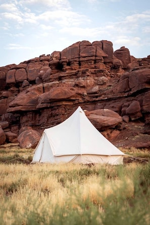 A white tent set up in a grassy field with a rocky mountain backdrop.