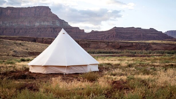 Une tente blanche se dresse dans un paysage naturel, avec des montagnes en arrière-plan.