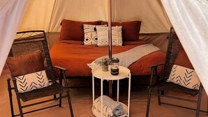 Een gezellige tent met een bed, twee stoelen en een kleine tafel met een lantaarn.