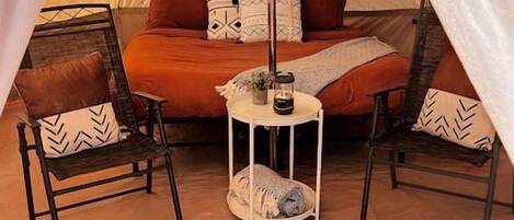 Une tente confortable avec un lit, deux chaises et une petite table sur laquelle est posée une lanterne.