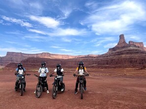 Three people on motorcycles in a desert landscape with red rock formations.