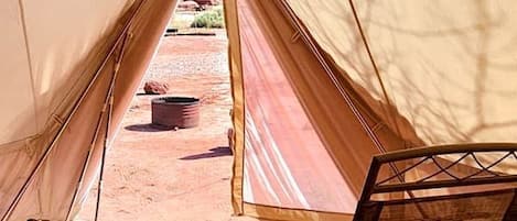 Una carpa con una cama, una silla y una mesita con una planta.