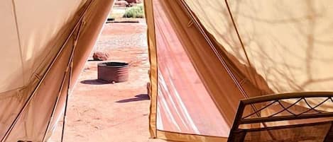 A tent with a bed, a chair, and a small table with a plant.