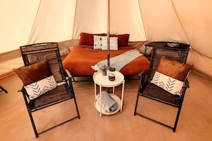 A tent with a bed, two chairs, a small table, and a floor lamp.