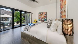 Une chambre moderne dotée d’un grand lit, d’un ventilateur de plafond et offrant une vue sur une piscine et un espace extérieur.
