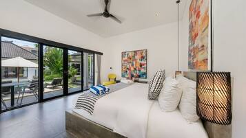 A modern bedroom with a large bed, a ceiling fan, and a view of a swimming pool and outdoor area.