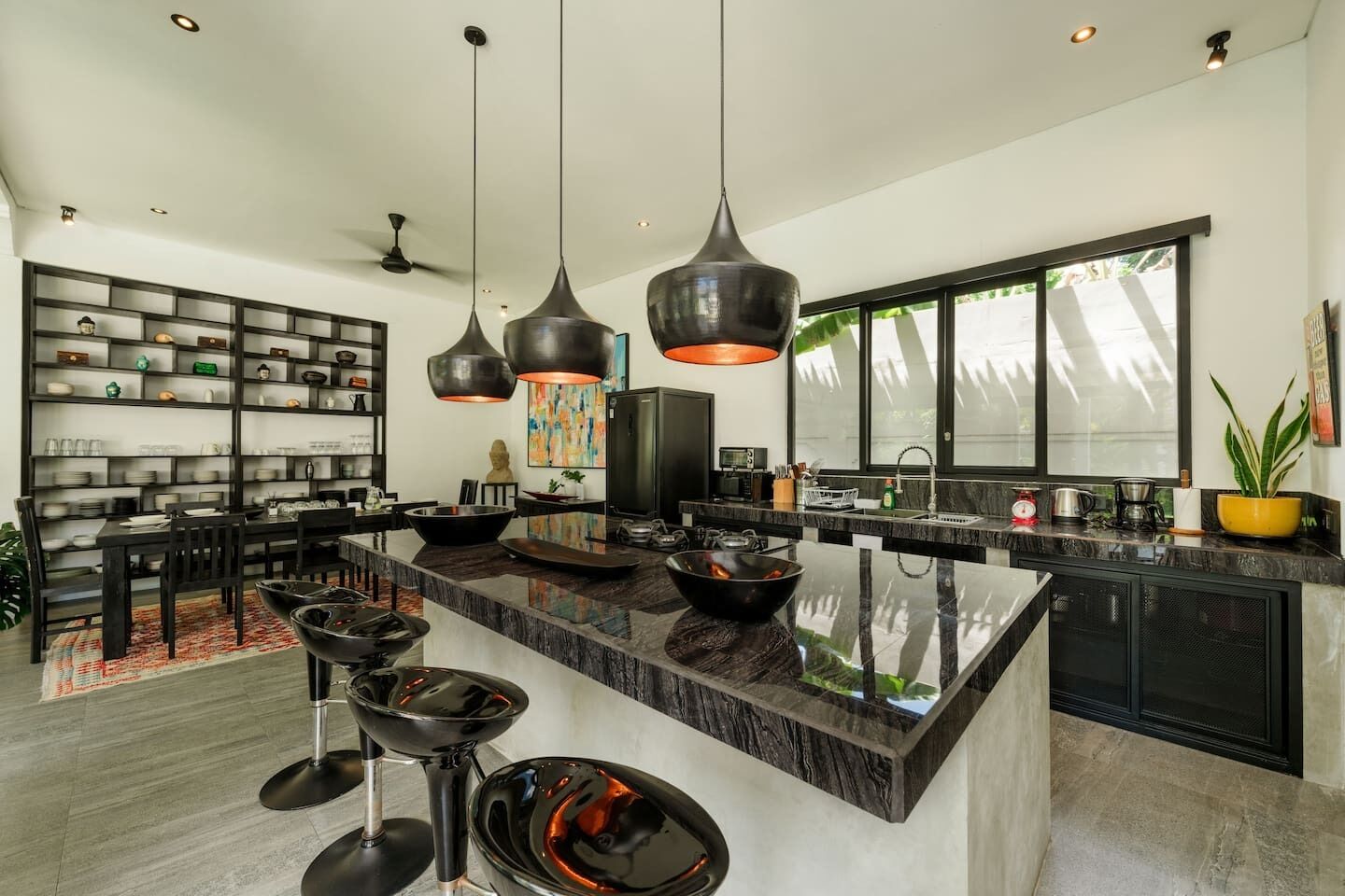 A modern kitchen with a large island, pendant lighting, and a dining area with a black dining set.