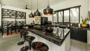 Une cuisine moderne dotée d’un grand îlot central, de luminaires suspendus et d’un coin repas avec un ensemble de salle à manger noir.