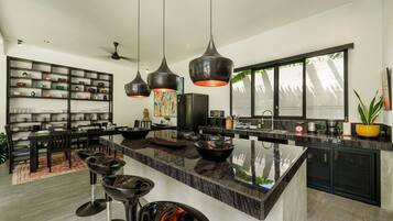 A modern kitchen with a large island, pendant lighting, and a dining area with a black dining set.