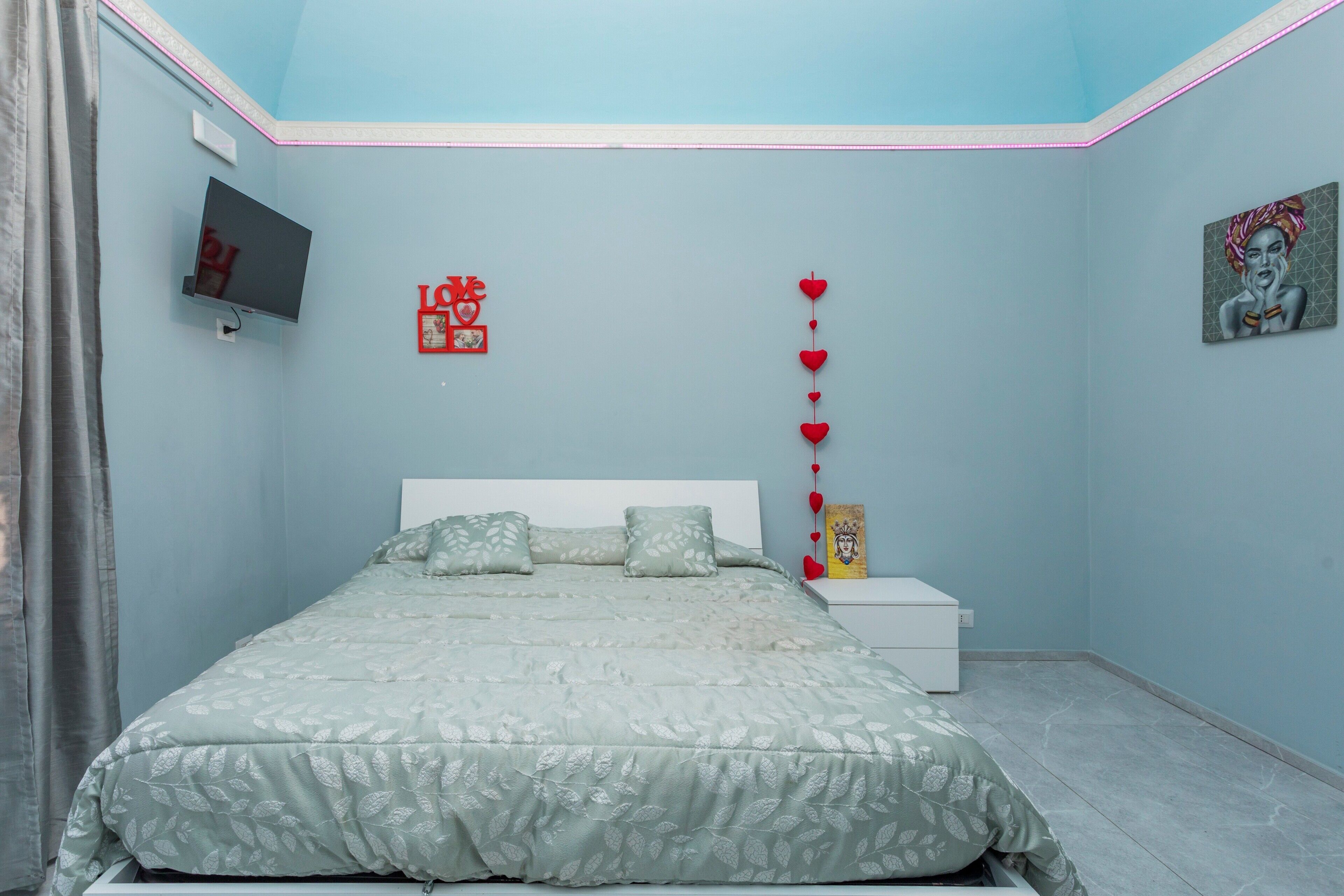 A bedroom with a bed, a TV, a nightstand, and a wall decoration.