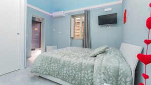 Una camera da letto con un letto, una TV, una finestra con tende e una porta che dà su un'altra stanza.