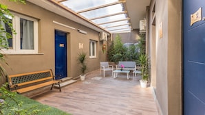 Un'area esterna coperta con panchine, sedie, un tavolo, piante in vaso e una porta blu.
