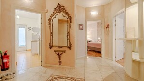 A hallway with a large ornate mirror, a fire extinguisher, and a patterned rug.