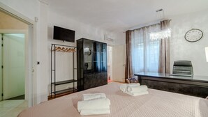 A hotel room with a bed, a TV, a desk, a chair, a coat rack, and a window with curtains.