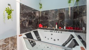 A modern bathroom with a marble wall, a glass-enclosed bathtub, and green plants. - Sp Luxury - Catania – Room 2 (Catania)